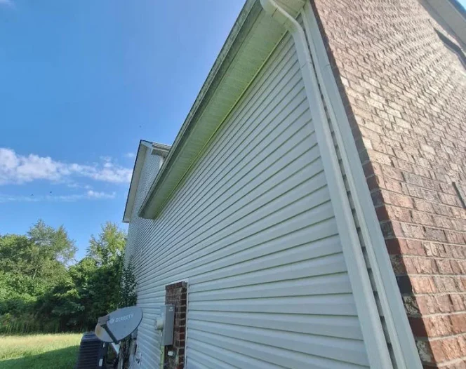 A house exterior with white siding and brick, a gray DIRECTV satellite dish, and green grass and trees.